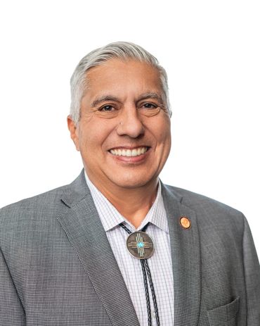 Smiling man in a gray suit with a bolo tie and white background.