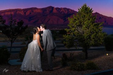 A young Gen-Z couple kissing at sunset with the Sandia Mountains in the background.
