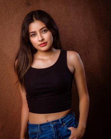 Young woman posing confidently against a textured brown wall.