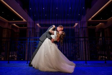 Bride and groom share a romantic dip and kiss under blue lights.