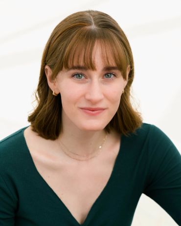 Young woman with light brown hair and green eyes smiling gently.