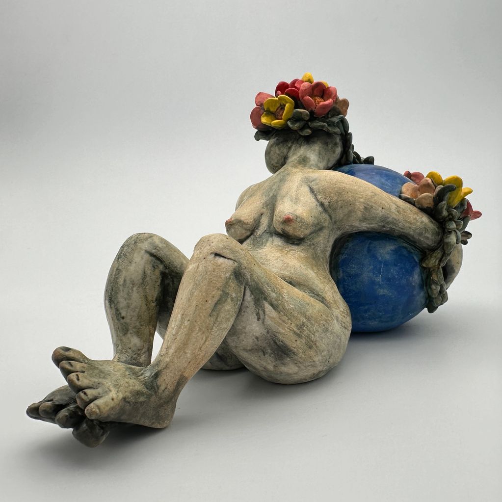 Sculpture of a reclining nude woman with floral crown and blue orb.