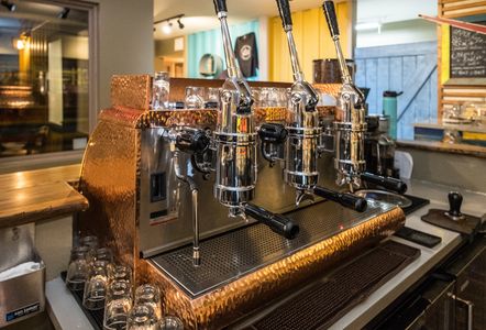 Copper espresso machine with lever pulls in a cafe setting.