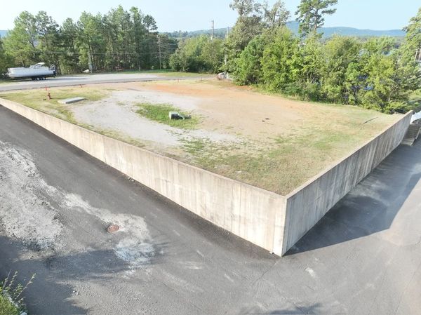 Empty lot surrounded by a tall concrete wall with trees in the background.