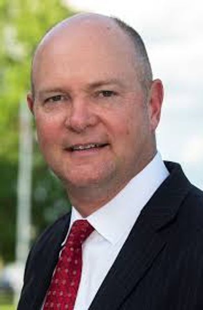 A professional man in a suit and red tie smiling outdoors.