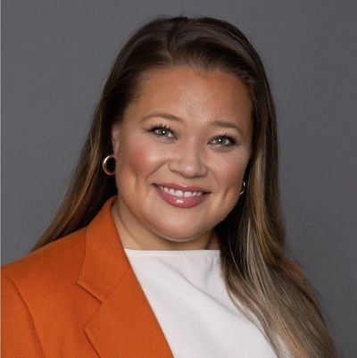 Smiling woman with long hair in an orange blazer and white top.