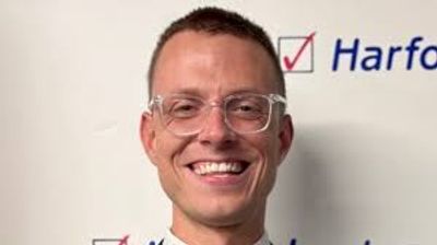 Smiling man wearing clear glasses in front of a whiteboard with text.