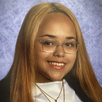 Young woman with long blonde hair and glasses smiling against a textured blue background.