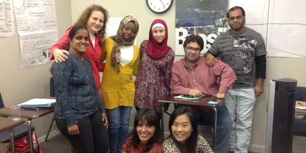 Diverse group of eight people posing happily in a classroom.