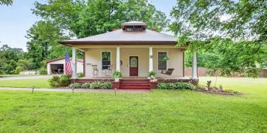 Small charming house with a large porch and lush green yard.