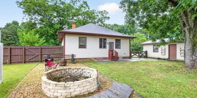 Backyard with a small house, fire pit, and green lawn.