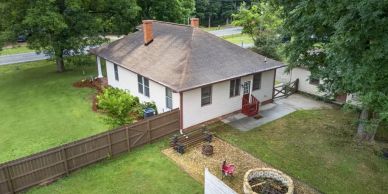 A white house with a brown roof and fenced backyard.