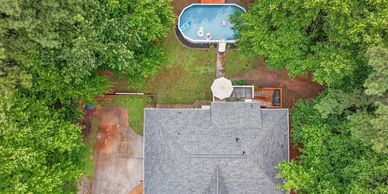 Aerial view of a house with a backyard pool surrounded by trees.