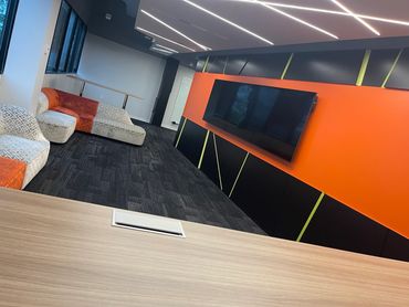 Modern office lounge with patterned sofas and a large TV on an orange and black wall.