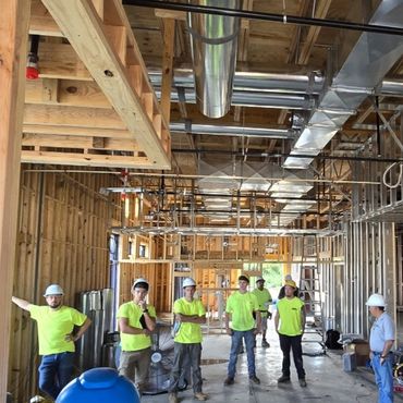 Construction workers in neon shirts and hard hats inside a building framework.
