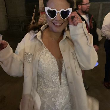 a bride in heart sunglasses and a coat over her wedding dress
