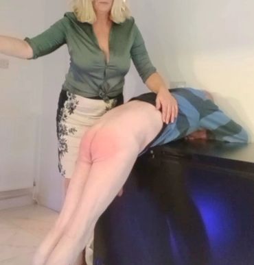 A woman spanking a man bent over a piece of furniture.
