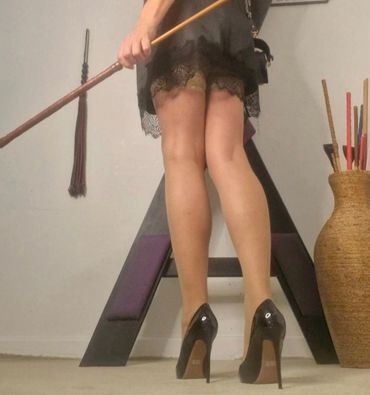 Woman in black high heels and lace dress holding a broomstick.