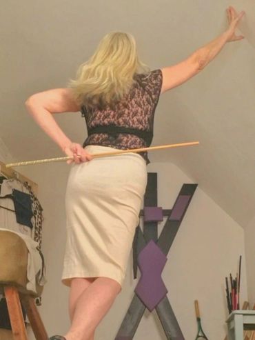 Woman in high heels and pencil skirt holding a cane, posing confidently indoors.
