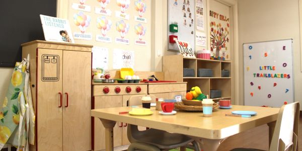 A colorful preschool classroom with play kitchen and learning materials.