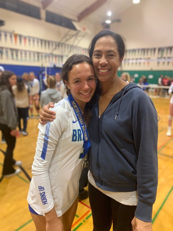 A proud athlete with a medal and a woman hugging her in a gym.