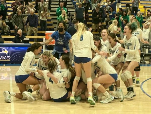 A volleyball team celebrates on the court after a win.