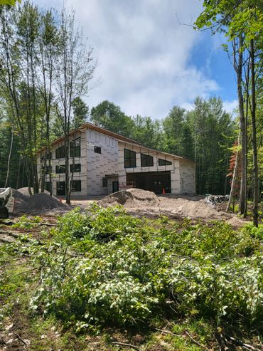 Modern house under construction surrounded by trees and building materials.