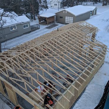 Wooden roof framework being constructed on a snowy site.