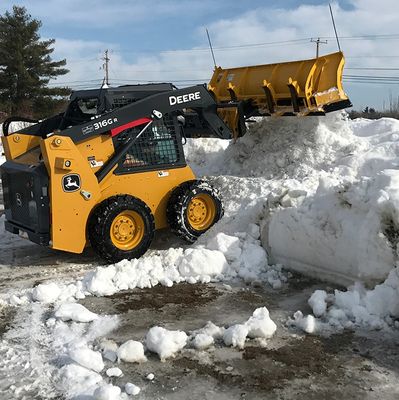 A yellow John Deere skid steer loader clearing snow.