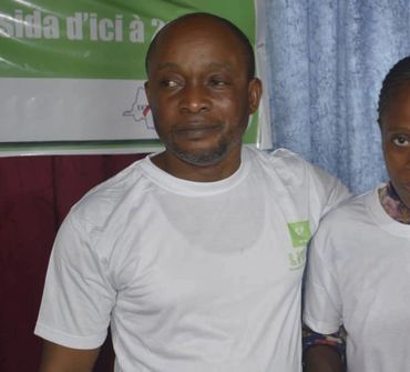 Man in a white t-shirt standing next to a woman with a blue curtain background.