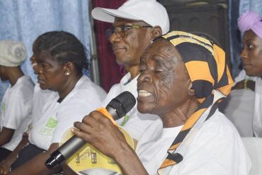 Elderly woman speaking into a microphone during a group event.