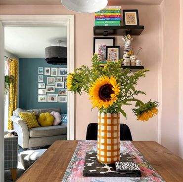 Sunflowers in checkered vase on dining table with cozy living room in background.