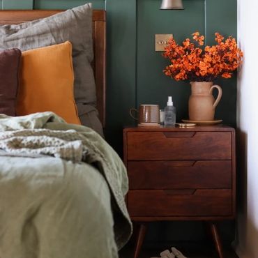 Cozy bedroom corner with green walls, wooden nightstand, orange flowers, and slippers.