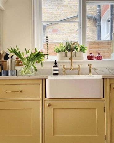 Cozy kitchen sink area with mustard cabinets, brass faucet, and fresh tulips.