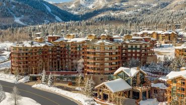 Snow-covered resort buildings surrounded by pine trees and mountains.