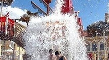 Children playing in a vibrant water park with slides and splash features under a sunny sky.