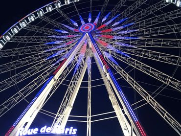Night view of the illuminated Roue de Paris Ferris wheel with red, white, and blue lights.