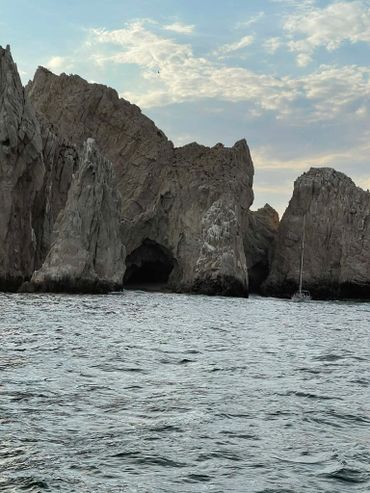 Rocky cliffs rise from the ocean under a partly cloudy sky with a boat nearby.