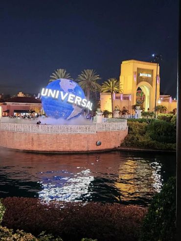 Night view of Universal Studios globe with illuminated entrance and reflections in water.