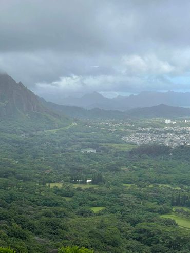 Cloudy mountain landscape with lush greenery and a distant town.