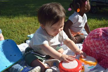 A toddler happily playing with toy drums outdoors on a sunny day.