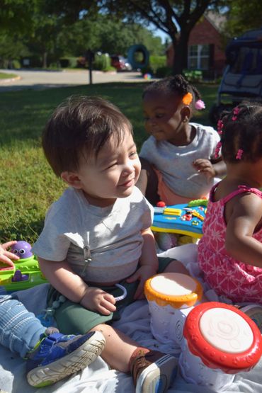 Toddlers playing with musical toys outdoors on a sunny day.
