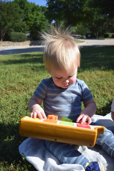 A toddler with messy hair playing with a colorful toy keyboard outdoors.