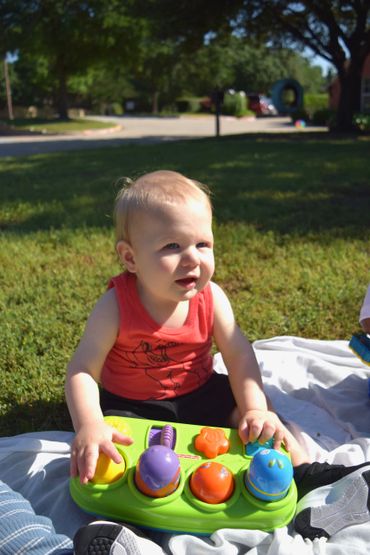 A toddler playing with a colorful toy outdoors on a sunny day.