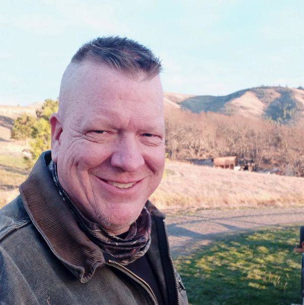 Smiling man outdoors with hills in the background.