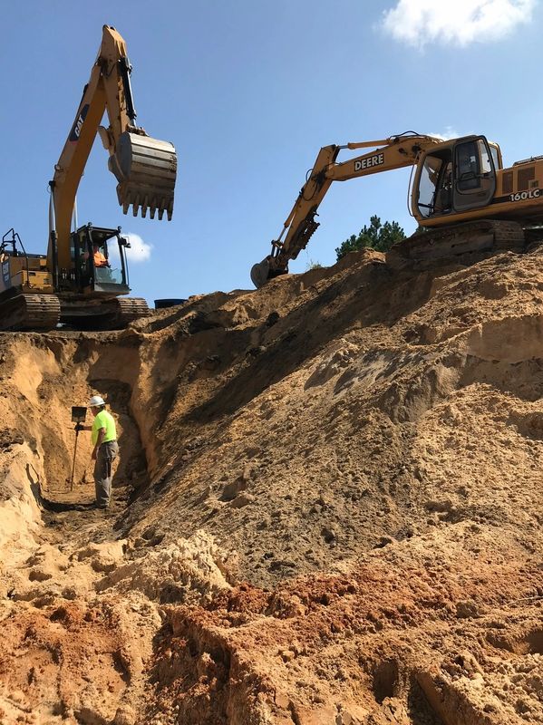 Two excavators digging a large trench with a worker inside.