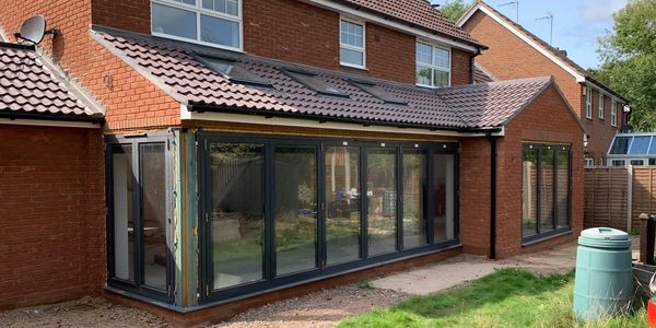 Newly installed black-framed glass folding doors on a brick house extension.