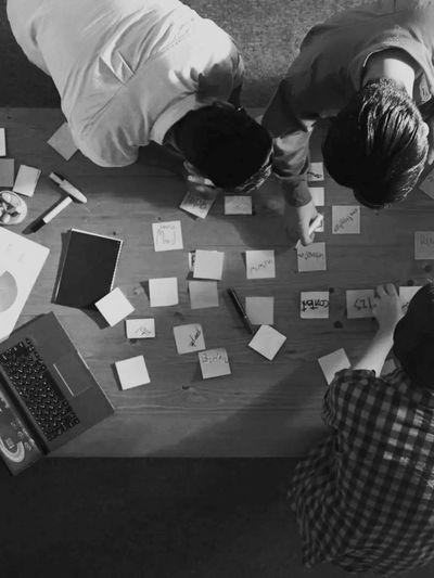 Three people brainstorming with sticky notes and a laptop on a wooden table.