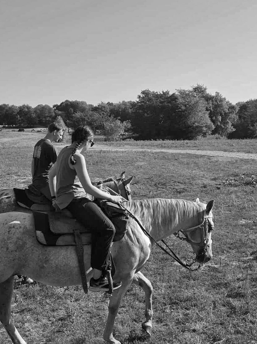 Couple riding a white horse on a sunny trail at Chisholm Trail Rides near Rockwall, Texas.