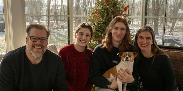 A happy family of four with their dog in front of a Christmas tree.
